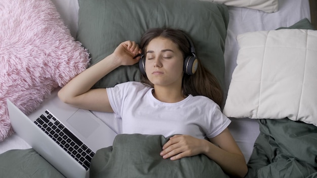 Porträt eines müden jungen Mädchens, das mit einem Laptop im Bett zu Hause schläft