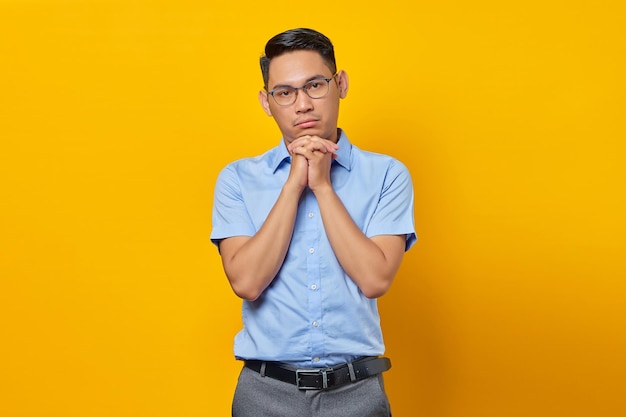 Porträt eines nachdenklichen jungen asiatischen Mannes mit Brille hält die Hand unter einem Kinn isoliert auf gelbem Hintergrund Geschäftsmann- und Unternehmerkonzept