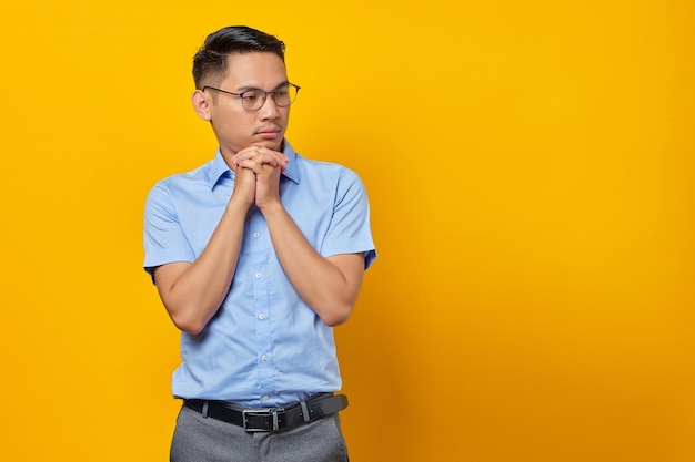 Porträt eines nachdenklichen jungen asiatischen Mannes mit Brille hält die Hand unter einem Kinn isoliert auf gelbem Hintergrund Geschäftsmann- und Unternehmerkonzept