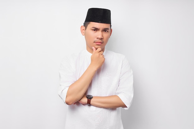 Porträt eines nachdenklichen jungen asiatischen muslimischen Mannes, der in die Kamera blickt und sein Kinn berührt und über ein Angebot nachdenkt, das auf weißem Hintergrund isoliert ist Menschen religiöses islamisches Lebensstilkonzept
