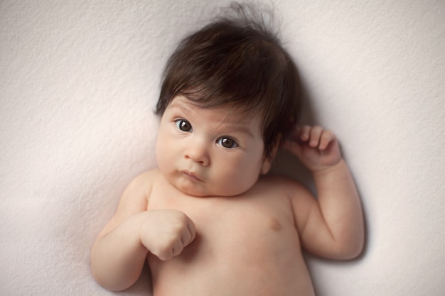 Porträt eines nackten ernsten Babys mit dunklem Haar und großen Augen