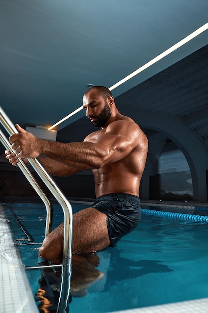 Porträt eines nassen sexy muskulösen Mannes, der im Swimmingpool steht