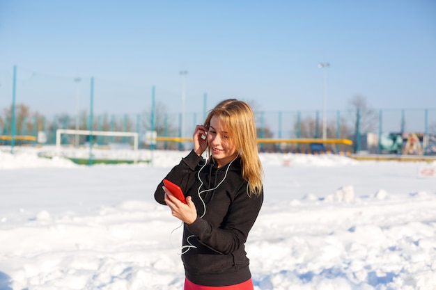 Porträt eines netten blonden Mädchens, das Musik beim ein rotes Telefon in der Hand halten hinunter die Straße gehen hört.