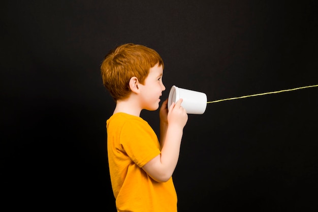 Porträt eines netten Jungen mit roten Haaren, der auf einem einfachen selbstgemachten Telefon spricht, der Junge spielt