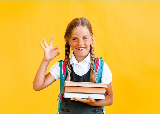 Porträt eines netten kleinen Mädchens auf gelbem Hintergrund. Das Schulmädchen schaut in die Kamera,