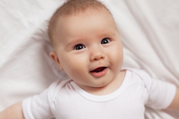 Porträt eines netten lächelnden neugeborenen Babys in einem weißen Bodysuit, Nahaufnahme Produkte für Kinder