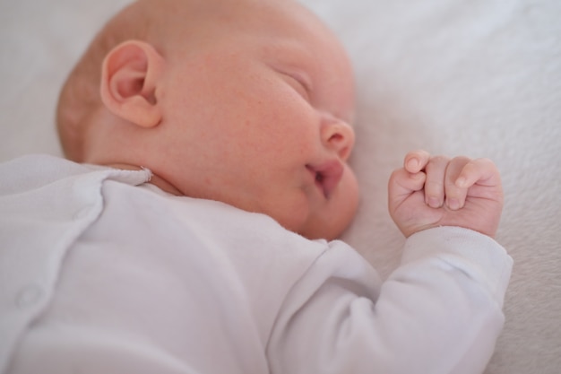 Porträt eines Neugeborenenbabys, das auf einer weißen Decke schläft.