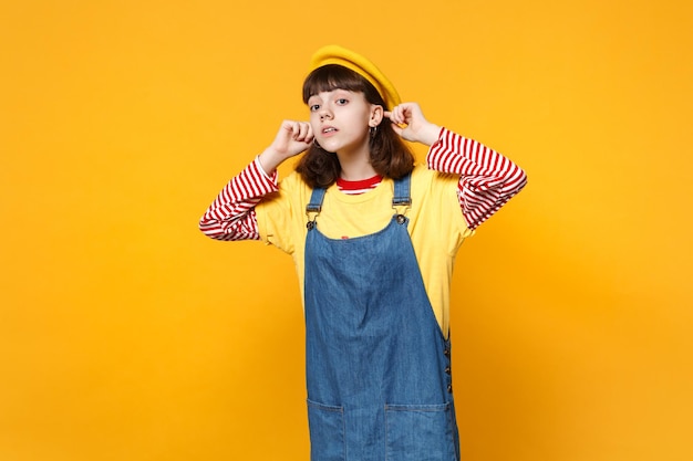 Porträt eines neugierigen Mädchen-Teenagers in französischer Baskenmütze, Denim-Sommerkleid, das aufmerksam in die Ferne blickt, isoliert auf gelbem Hintergrund. Menschen aufrichtige Emotionen, Lifestyle-Konzept. Mock-up-Kopienbereich.