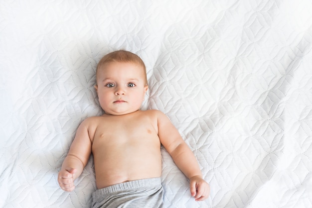 Foto porträt eines niedlichen babys von neun monaten. kleiner junge beobachtet mit interesse, was auf dem bett passiert