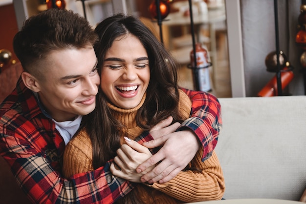 Porträt eines niedlichen jungen glücklichen liebenden Paares, das im Café drinnen umarmt sitzt.