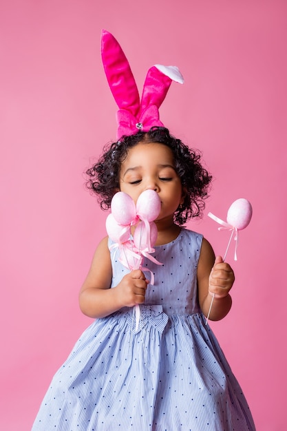 Porträt eines niedlichen kleinen Mädchens mit Osterhasenohren auf ihrem Kopf, der Ostereier hält. Studio, rosa Hintergrund