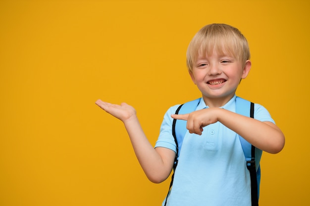 Porträt eines niedlichen Schuljungen 6 Jahre alt mit einem hellen Rucksack auf einem gelben Hintergrund. Zurück zur Schule.