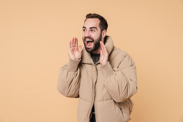 Porträt eines optimistischen Mannes in Winterjacke, der im Exemplar einzeln auf Beige ruft oder schreit