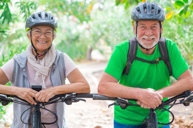 Porträt eines Paares alter und glücklich verliebter Senioren, die lächelnd in die Kamera schauen und Spaß mit ihren Fahrrädern in der Natur im Freien haben, die sich gemeinsam gut und gesund fühlen xA