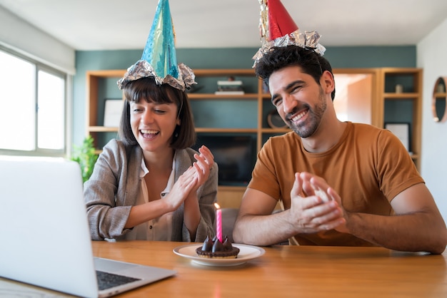 Porträt eines Paares, das Geburtstag auf einem Videoanruf mit einem Laptop von zu Hause feiert. Paar feiert Geburtstag online in Quarantänezeit. Neues normales Lifestyle-Konzept.