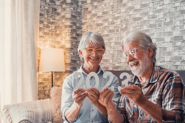 Porträt eines Paares von zwei alten Rentnern, die zu Hause die Zahlen von 2023 zusammenhalten Nahaufnahme der Neujahrszahlen, die feiern, und Ziele für ein neues Lebenskonzept