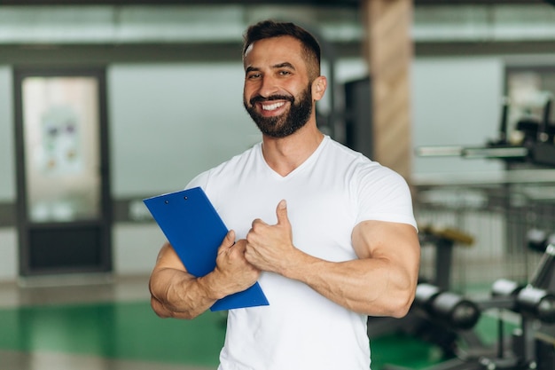 Foto porträt eines persönlichen trainers mit klemmbrett mit trainingsplan im fitnessstudio