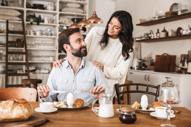 Porträt eines positiven Paares Mann und Frau, die am Tisch essen, während sie in der Küche zu Hause frühstücken