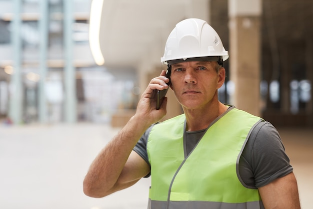 Porträt eines professionellen Bauarbeiters, der telefonisch und auf der Baustelle steht,