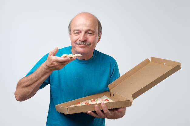 Porträt eines reifen europäischen Mannes, der ein Stück Pizza isst In seinen Händen hält er eine Schachtel mit Essen Studio-Shooting