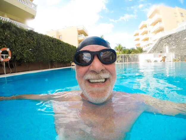 Porträt eines reifen Mannes, der lächelt und die Kamera im Pool anschaut und allein Spaß hat - Training und Schwimmen glücklich - Nahaufnahme des Gesichts eines glücklichen Seniors