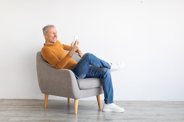 Porträt eines reifen Mannes mit Smartphone auf einem Sessel sitzend