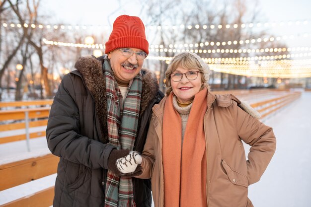 Porträt eines reifen Paares, das am Wintertag in die Kamera lächelt, während es im Park spazieren geht