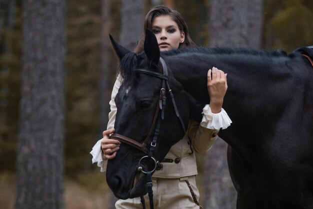 Porträt eines Reiters in einem Retro-Anzug und ihrem schwarzen Pferd eine junge Brünette nimmt Kontakt mit einem Pferd auf