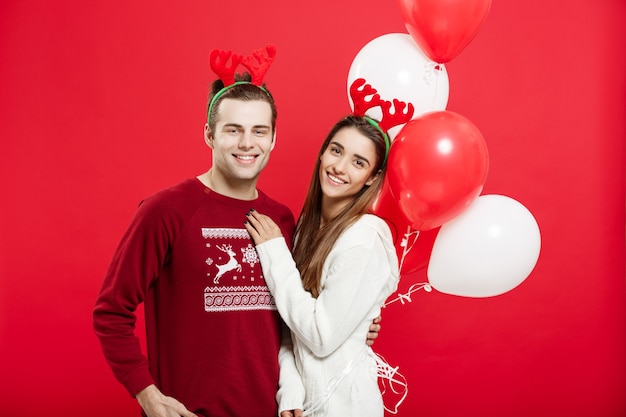 Porträt eines romantischen jungen Paares mit Weihnachtsballon über rotem Studiohintergrund.