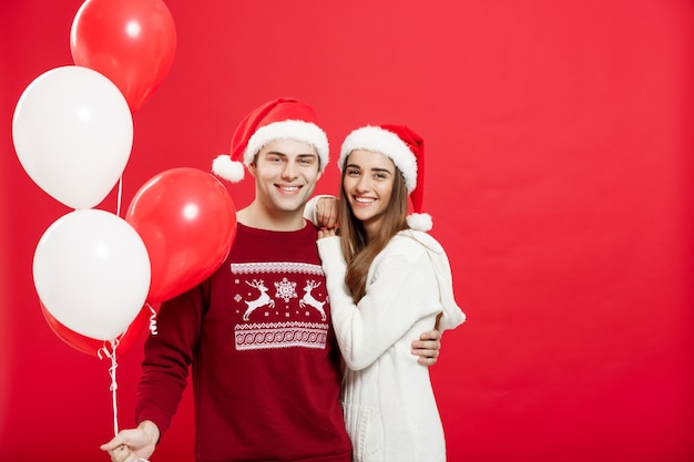 Porträt eines romantischen jungen Paares mit Weihnachtsballon über rotem Studiohintergrund.