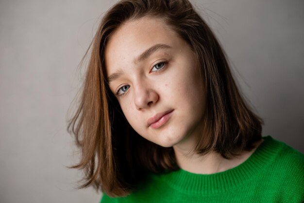 Porträt eines schlanken Mädchens im Teenageralter in einem grünen Pullover bei natürlichem Licht vor einer weißen Ziegelwand. Natürliche Schönheit, kein Make-up. Problemhaut. Platz für Text. Foto in hoher Qualität
