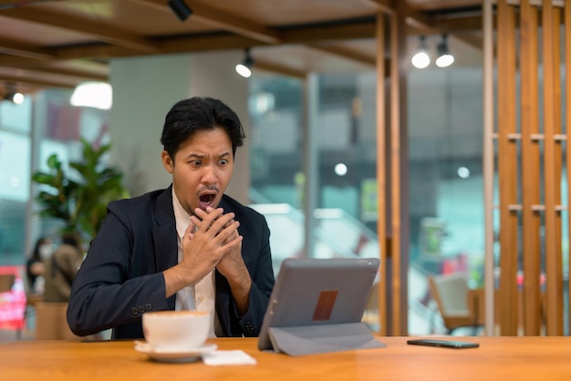 Porträt eines schockierten asiatischen Geschäftsmannes im Café mit digitalem Tablet-Computer