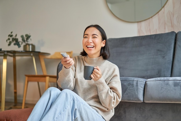 Porträt eines schönen asiatischen Mädchens, das bei ihr zu Hause sitzt und fernsieht und fern lächelt und lacht