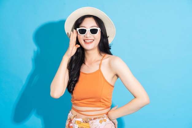 Porträt eines schönen asiatischen Mädchens im Badeanzug, das glücklich auf blauem Hintergrund lächelt