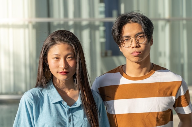 Porträt eines schönen asiatischen Paares, das im Freien auf dem Studentencampus während einer sonnigen Zeit in die Kamera schaut