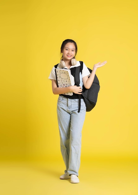 Porträt eines schönen asiatischen Schulmädchens mit Rucksack auf gelbem Hintergrund xA