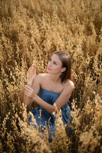 Porträt eines schönen brünetten Mädchens in einem blauen Kleid auf einem gelben Feld mit Weizen im Dorf