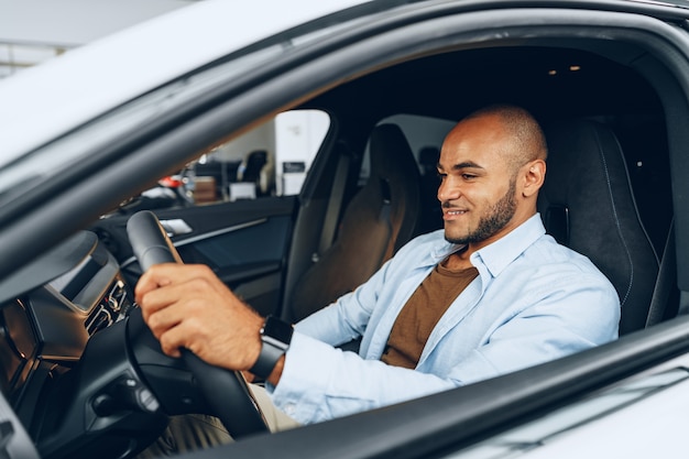 Porträt eines schönen glücklichen Afroamerikaners, der in seinem neu gekauften Auto Nahaufnahme sitzt