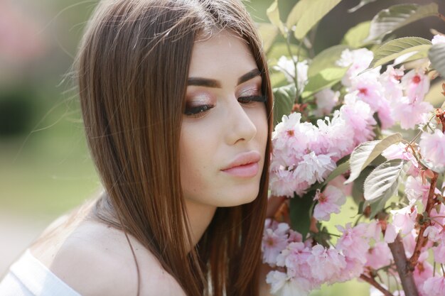 Porträt eines schönen jungen Frauenmodells nahe rosa Zweigen mit Sakura-Blumen