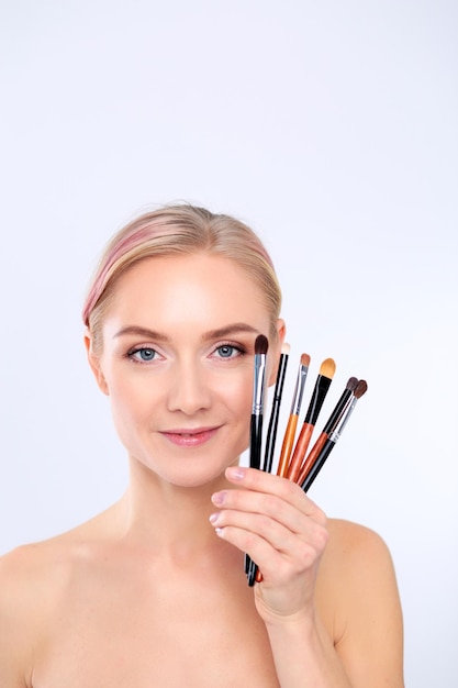 Porträt eines schönen jungen Mädchens auf weißem Hintergrund mit einem perfekten Gesicht mit vielen Händen, die Make-up-Pinsel halten