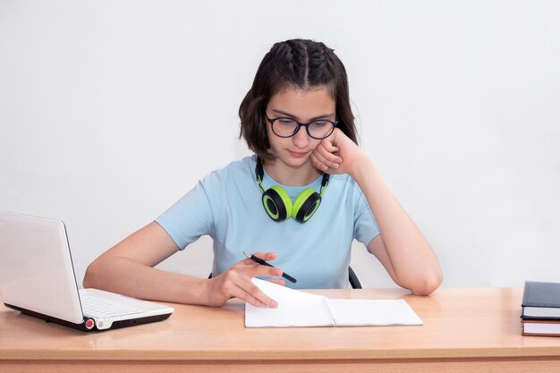 Porträt eines schönen jungen Mädchens, das an einem Tisch sitzt, Hausaufgaben macht oder sich auf eine Prüfung auf weißem Hintergrund vorbereitet. Online-Lernkonzept