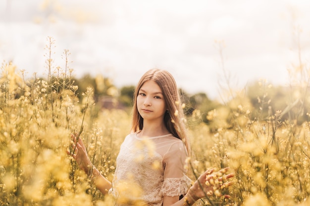 Porträt eines schönen jungen Mädchens mit langen Haaren vor dem Hintergrund von Rapsblumen. Jugend und Natur