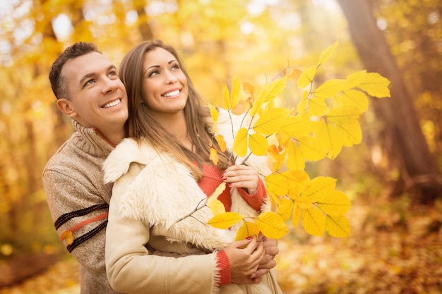 Porträt eines schönen jungen Paares im sonnigen Wald in Herbstfarben. Sie sind umarmt und halten gelbes Blatt.