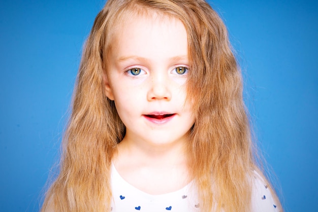 Porträt eines schönen kleinen Mädchens mit langen blonden Haaren auf blauem Hintergrund im Studio