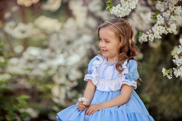 Porträt eines schönen lachenden Prinzessinnenmädchens in einem blauen Kleid für einen Spaziergang in einem blühenden Frühlingsgarten