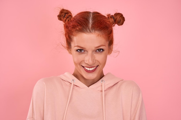Porträt eines schönen lächelnden rothaarigen jungen weiblichen Mädchens im Hoodie auf rosa Hintergrund im Studio