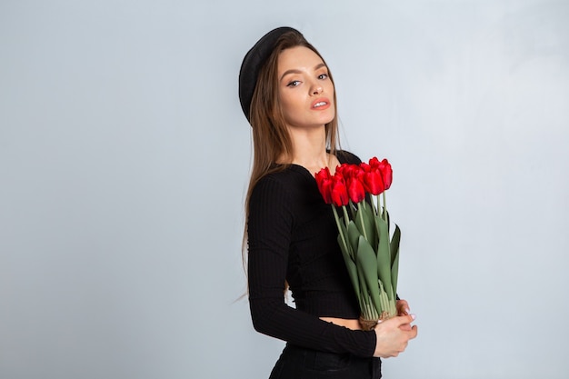 Porträt eines schönen Mädchens in einem Hut mit Tulpen in den Händen im Studio