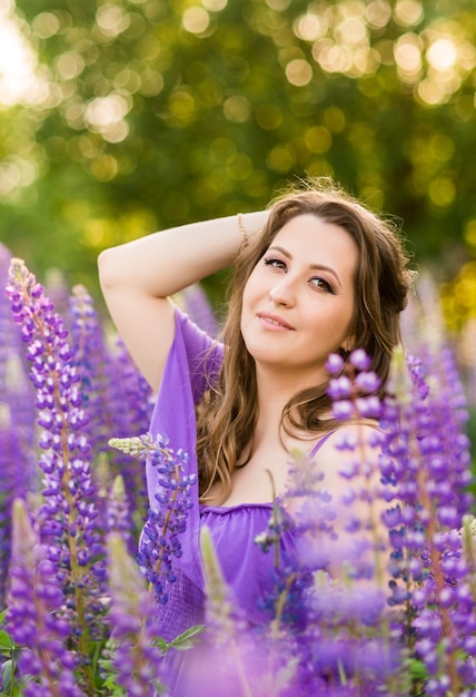 Porträt eines schönen Mädchens in einem lila Sommerkleid Eine Frau auf dem Hintergrund von Lupinen genießt Sommer und Natur