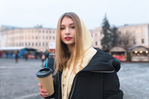 Porträt eines schönen Mädchens in einer Jacke mit einer Tasse Kaffee in ihren Händen