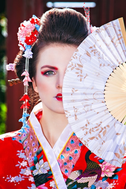 Porträt eines schönen Mädchens in Geisha-Kostüm mit ausgefallenem Make-up mit einem Fan